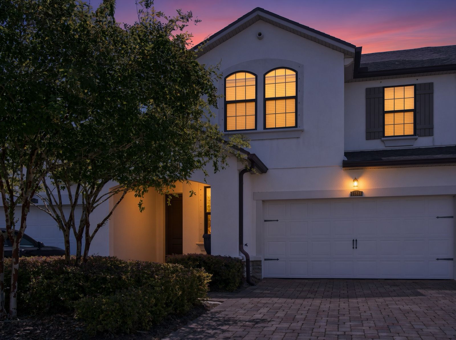 Twilight exterior of a South Florida home with warmly lit windows and paver driveway